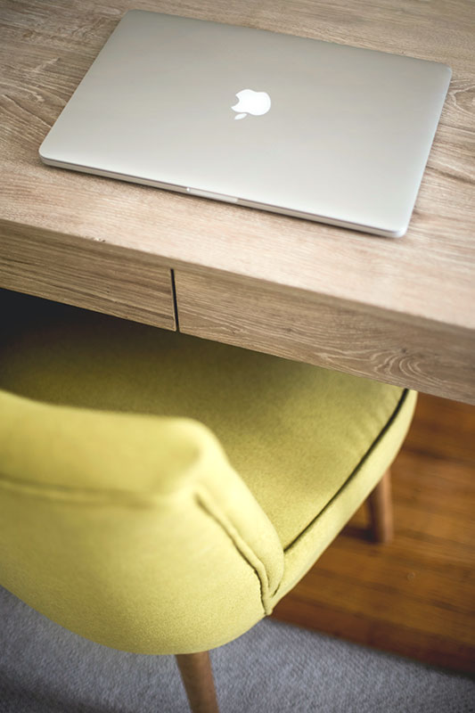 Closed macbook on a wooden desk with a yellow chair. 