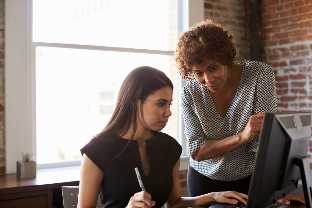 Woman at computer being mentored by standing woman